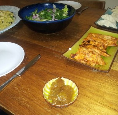 Image of a table with plates of tandoori chicken, pappadums, indian rice and salad on it